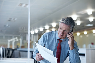 Buy stock photo Shot of a senior businessman reading a document while on the phone