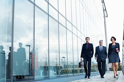 Buy stock photo Shot of three businesspeople walking and talking next to an office building