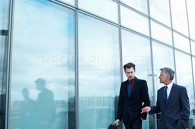 Buy stock photo Shot of two businessmen walking and talking next to an office building
