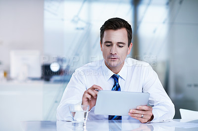 Buy stock photo Shot of a businessman sitting in an office using a digital tablet