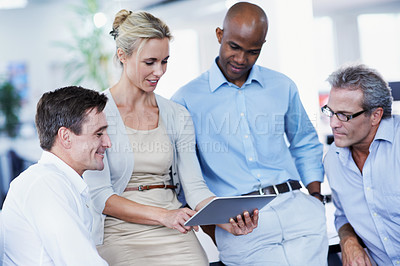 Buy stock photo Shot of a diverse group of businesspeople looking at a digital tablet while standing in an office