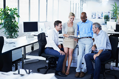 Buy stock photo Shot of a diverse group of businesspeople looking at a digital tablet while standing in an office