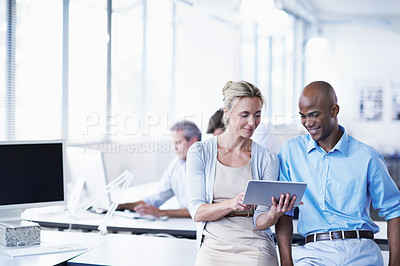Buy stock photo Shot of two office workers looking at a digital tablet with coworkers in the background