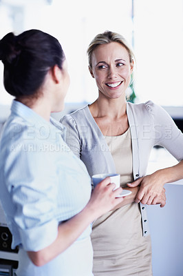 Buy stock photo Shot of two female coworkers chatting over a coffee in an office