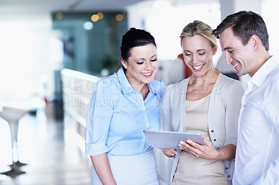 Buy stock photo Shot of three coworkers looking at a digital tablet while standing in an office