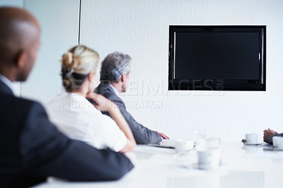 Buy stock photo Shot of a group of businesspeople sitting around a boardroom table looking at a blank monitor