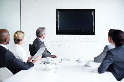 Buy stock photo Rearveiw shot of a diverse group of businesspeople sitting around a boardroom table looking at a blank monitor