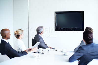 Buy stock photo Shot of a group of businessmen and businesswomen sitting around a boardroom table looking at a blank monitor