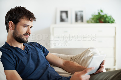 Buy stock photo A handsome young man using his tablet while sitting at home