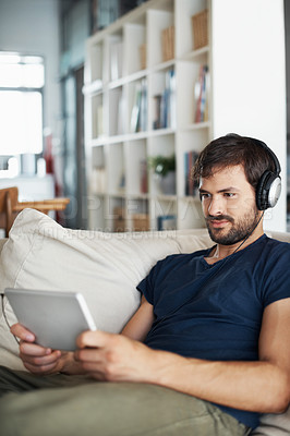 Buy stock photo A handsome young man listening to music on his tablet while sitting at home