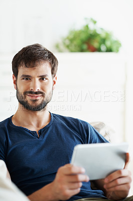 Buy stock photo Portrait of a handsome young man using his tablet while sitting on the sofa