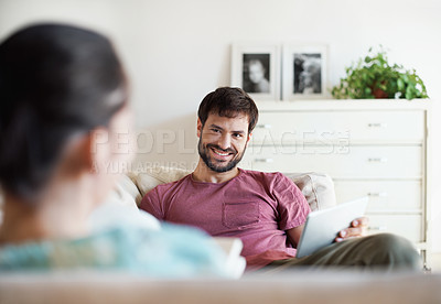 Buy stock photo A handsome young man using his tablet while his wife reads a book