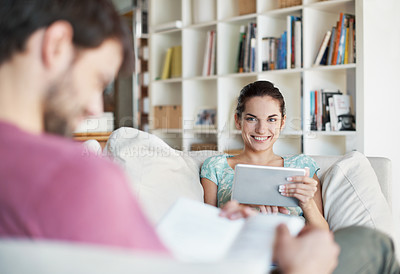 Buy stock photo Portrait of a beautiful young woman using her tablet while her husband reads a book