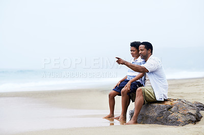 Buy stock photo An African-American father and son sitting by the sea on an overcast day