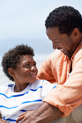 Buy stock photo An African-American father and his son sitting by the sea on an overcast day