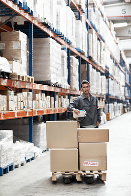 Buy stock photo Portrait of a young man using a pallet truck to transport boxes in a warehouse