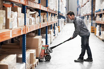 Buy stock photo A young man using a pallet truck to pack boxes in a storehouse