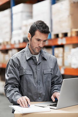 Buy stock photo A young man using his notebook and taking notes while working in a warehouse
