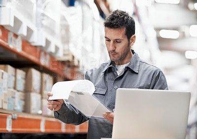 Buy stock photo A young man using his notebook and checking his notes while working in a storehouse