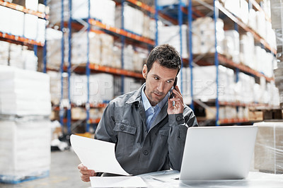 Buy stock photo A young man in a warehouse taking orders on his cellphone and recording them on his laptop
