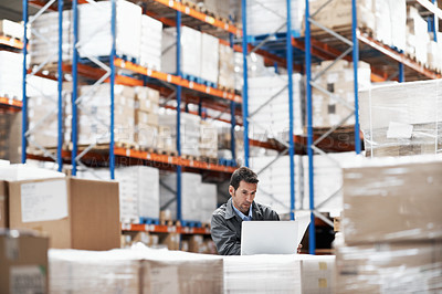 Buy stock photo A handsome young man using his laptop while working in a warehouse