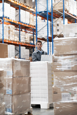 Buy stock photo Portrait of a handsome young man working on his notebook while sitting in a warehouse