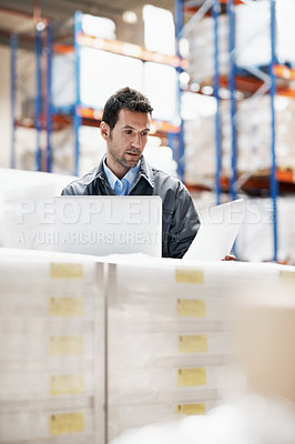 Buy stock photo A young man using his notebook and checking his notes while working in a storehouse