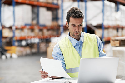 Buy stock photo A young man using his notebook and checking his notes while working in a warehouse