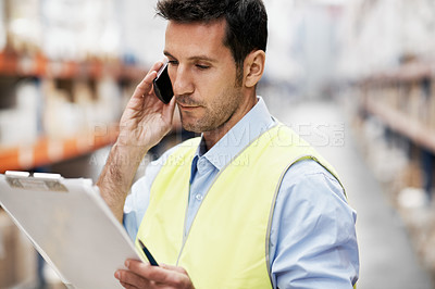 Buy stock photo A young man in a warehouse taking orders on his cellphone