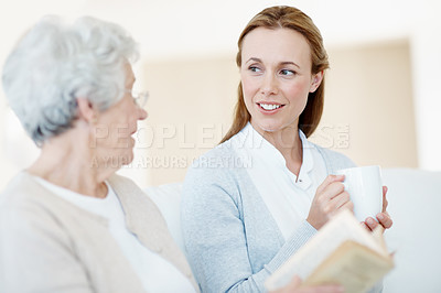 Buy stock photo Book, coffee and mother with old woman for care, bonding together and conversation in home. Novel, elderly parent and adult daughter with drink in living room, gossip story and happy family with love