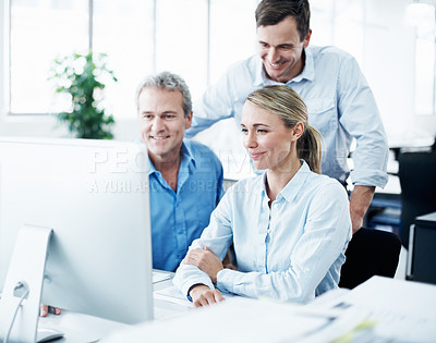 Buy stock photo Three businesspeople looking at a computer screen while working together in their office