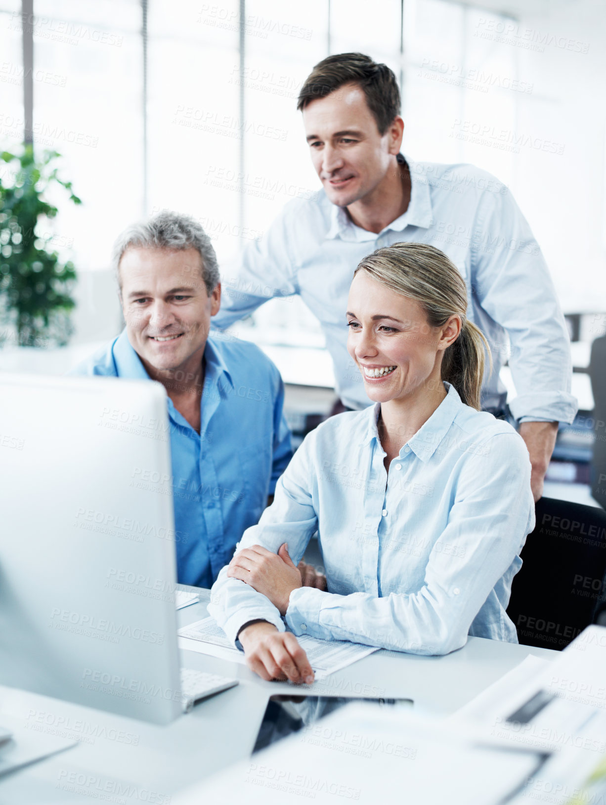 Buy stock photo Three businesspeople looking at a computer screen while working together in their office