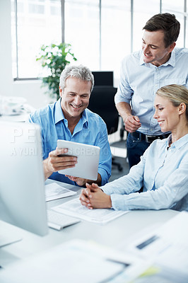 Buy stock photo Three businesspeople looking at a digital tablet while working together in their office