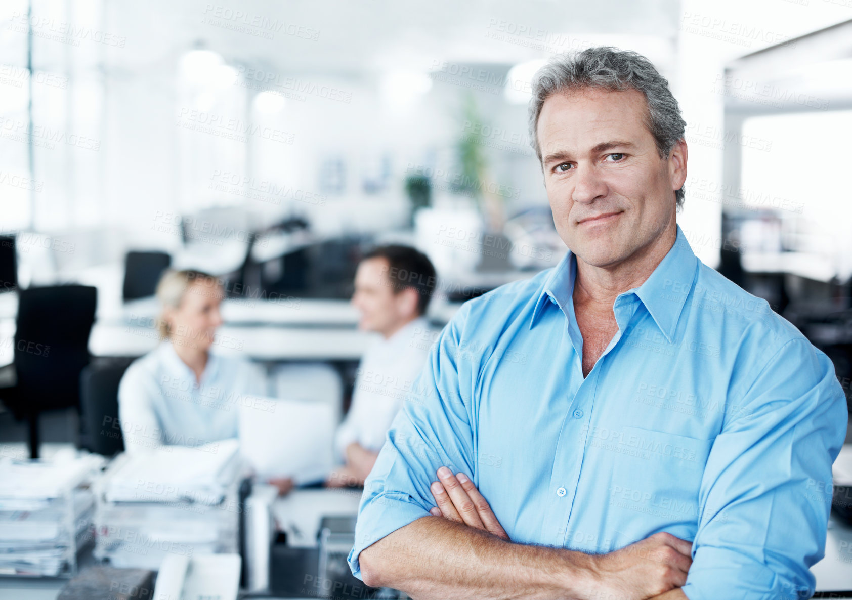 Buy stock photo Confident mature businessman sitting on a desk with his coworkers in the background
