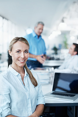Buy stock photo Portrait of a beautiful young businesswoman sitting at her desk with her colleagues in the background