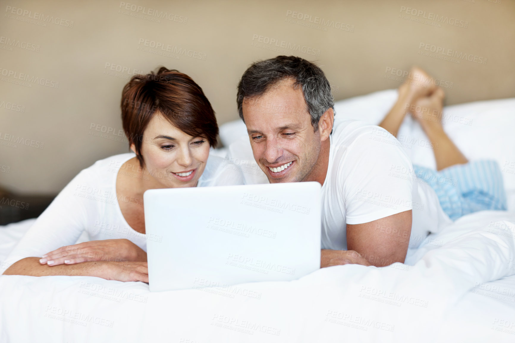 Buy stock photo Reading, laptop and couple together on bed with love, care and bonding with comfort and web in home. Happy man, woman and tech in bedroom with internet connection, streaming online and subscription