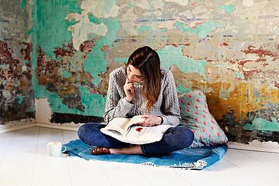 Buy stock photo Shot of a young woman reading a book on the floor of her apartment