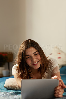 Buy stock photo Shot of a young woman relaxing with a digital tablet on her bed