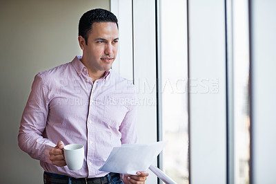 Buy stock photo Shot of a businessman holding paperwork while standing by an office window
