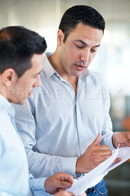 Buy stock photo Shot of two male colleagues discussing paperwork in the office