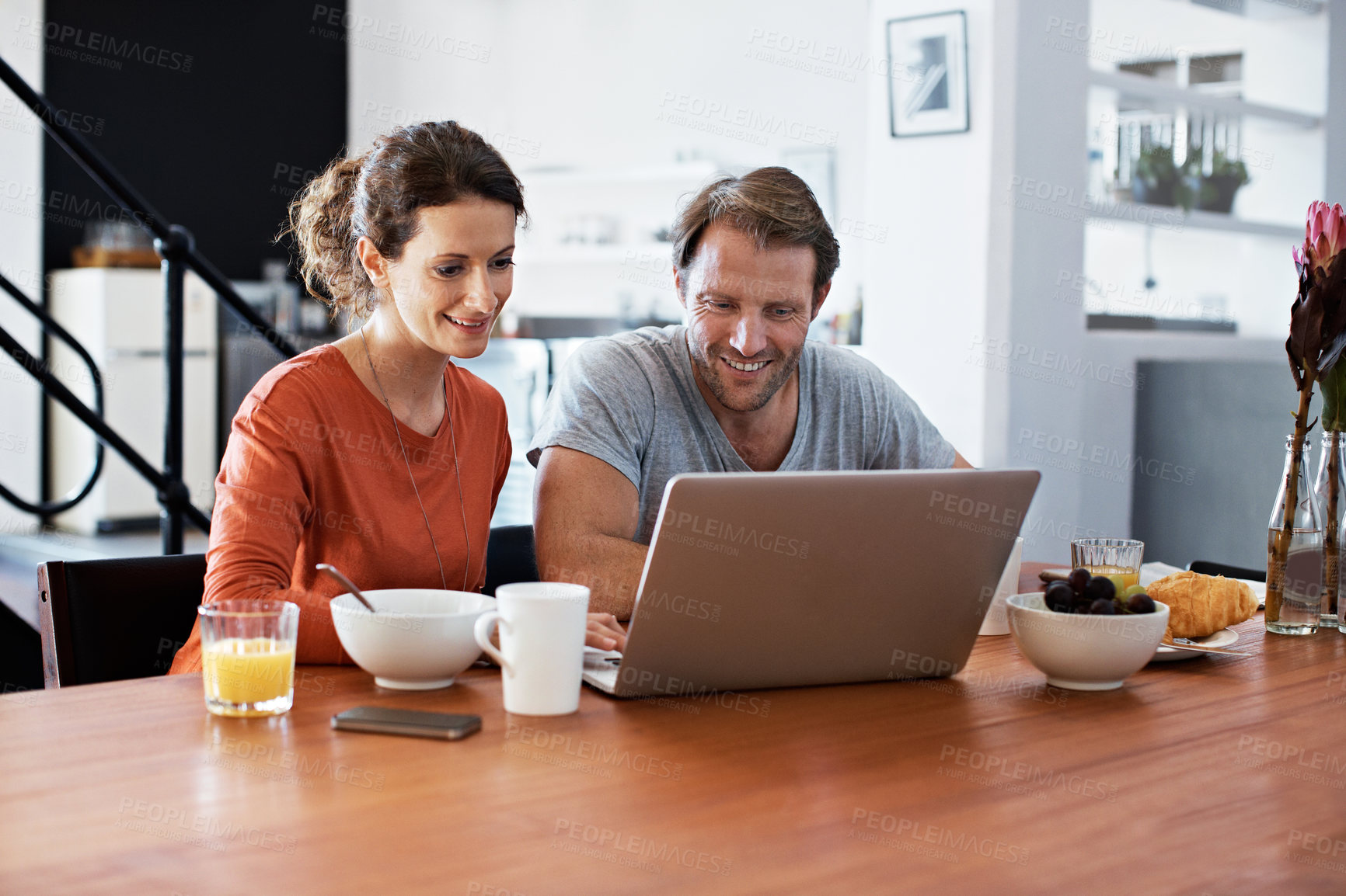 Buy stock photo Shot of a couple sitting at the dining table eating breakfast and using a laptop