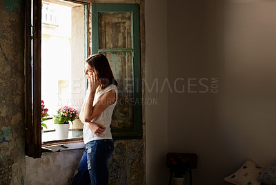 Buy stock photo Shot of a young woman talking on her cellphone while looking out of a window