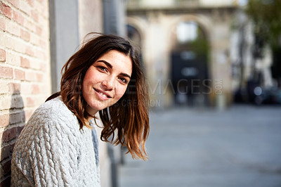 Buy stock photo Portrait of a smiling young woman leaning against a brick wall outside