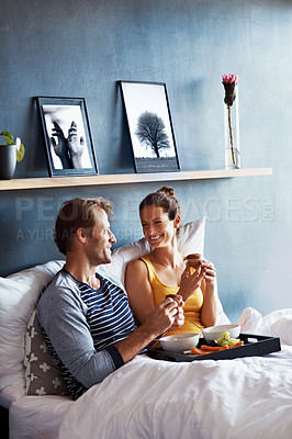 Buy stock photo Shot of a content couple sitting in bed together eating breakfast