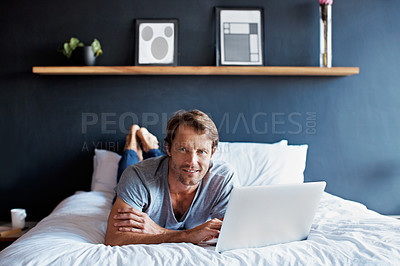 Buy stock photo Portrait of a mature man lying on his bed using a laptop