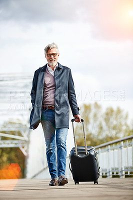 Buy stock photo Shot of a mature man pulling a suitcase while walking over a bridge in the city