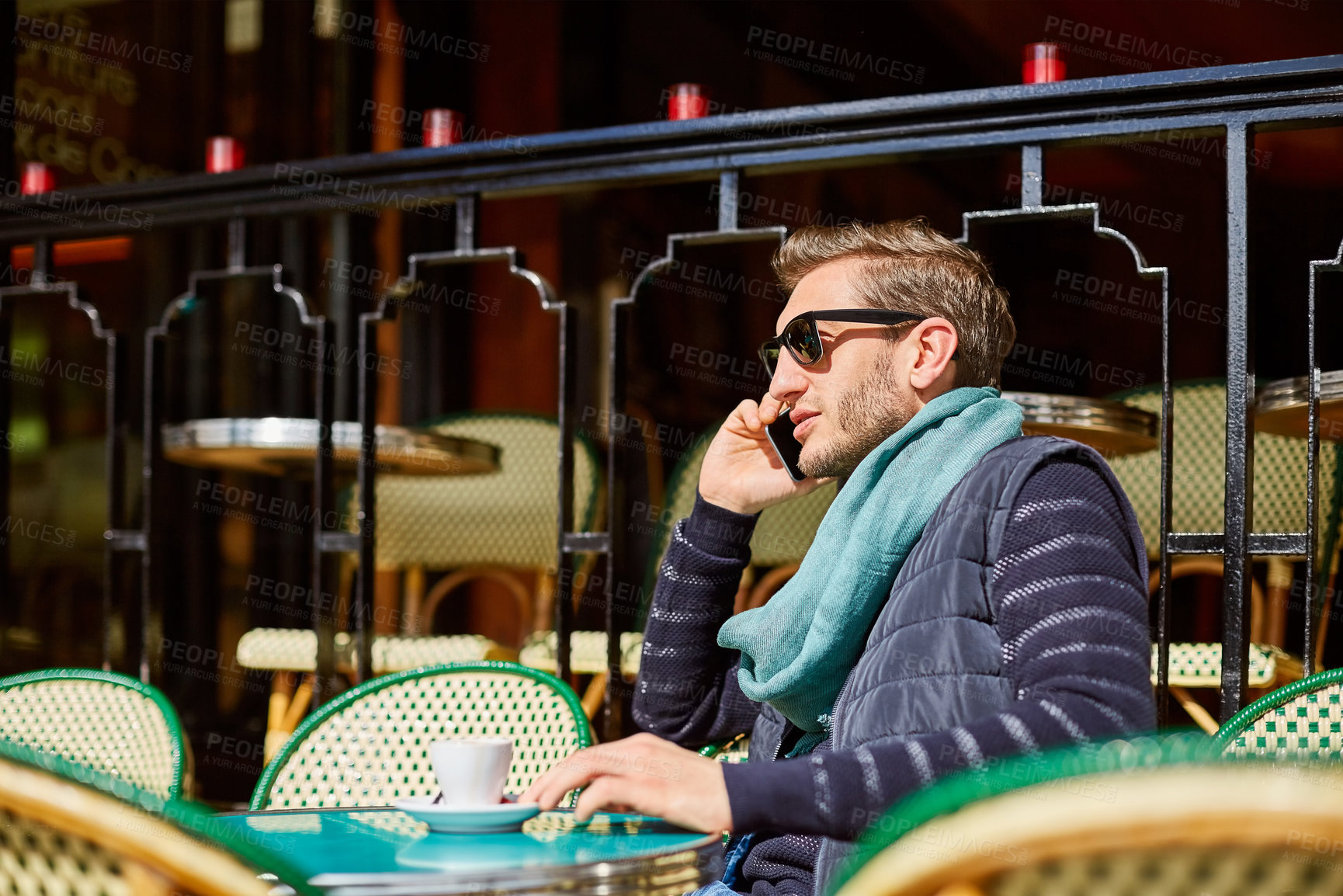 Buy stock photo Shot of a young man sitting at a sidewalk cafe in Paris talking on a cellphone
