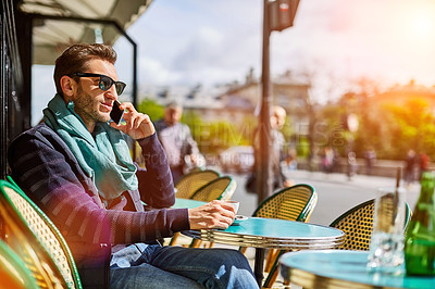 Buy stock photo Shot of a young man sitting at a sidewalk cafe in Paris talking on a cellphone