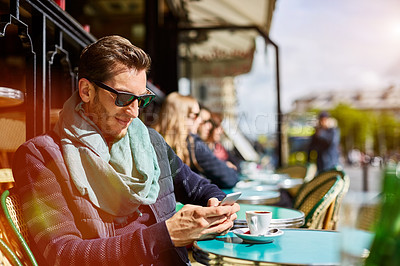 Buy stock photo Shot of a young man sitting at a sidewalk cafe in Paris reading a text on a cellphone