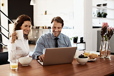 Buy stock photo Shot of a professional couple sitting at the dining table eating breakfast and using a laptop